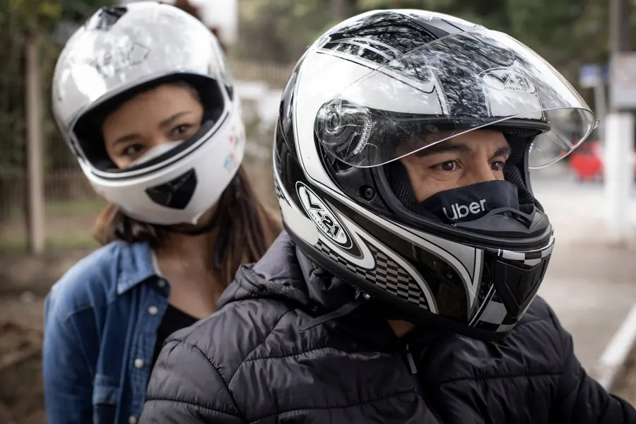 Motorista de aplicativo de moto com passageira, ambos de capacete