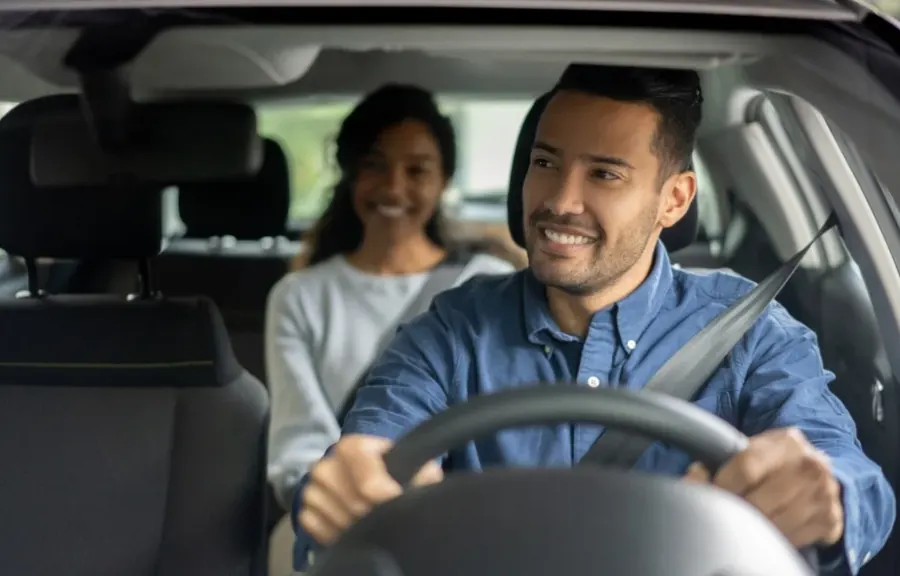 Motorista de aplicativo sorrindo ao volante com passageira no banco de trás